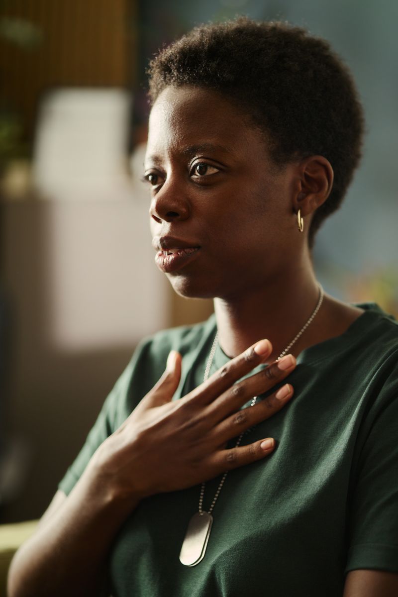 A woman wearing dog tags rests her hand on her chest as she talks.